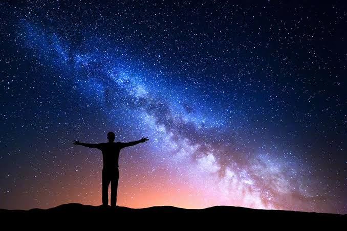 A star-filled night sky above a silhouetted figure standing on a ridge