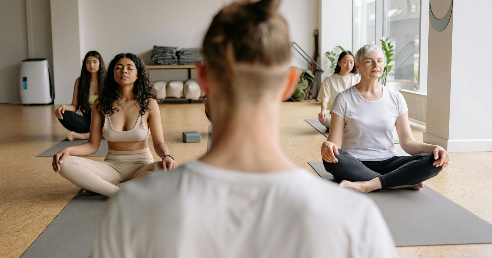A teacher leading a seated meditation during a group class in a bright studio